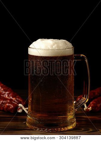 A Pint Of Light Beer And Sausage On A Wooden Table.