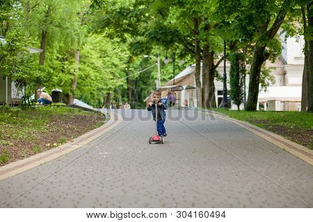 Little Boy Riding Scooter In City Park In Aummer. Kids Sports Outdoors. Happy Child Playing With His