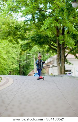 Little Boy Riding Scooter In City Park In Aummer. Kids Sports Outdoors. Happy Child Playing With His