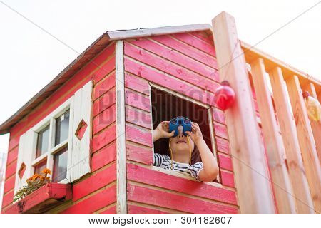 Boy in a wooden playhouse looking through a binocular
