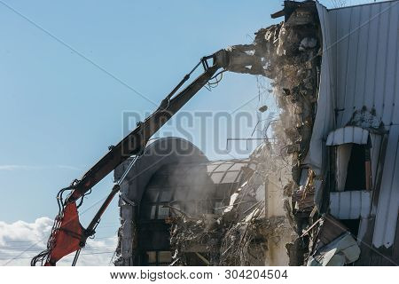 Excavator With Long Mechanical Arm At Height Breaks Off Pieces Of The House. Cleaning Area For A New