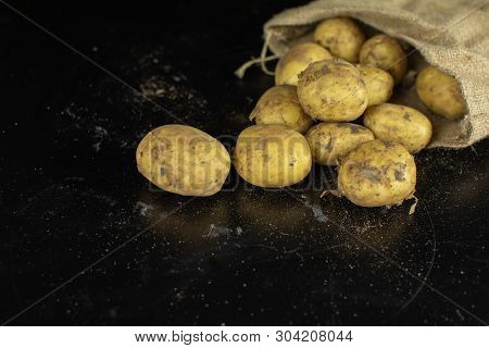 Potatoes On Black Surfase In A Canvas Bag. Fresh Potato With Traces Of Earth On The Skin. Dirty Raw 