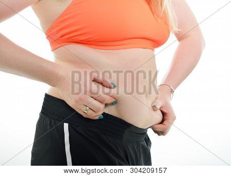 Overweight young woman shows belly fat, isolated over white background. Overeating xl size girl unhappy with her figure and overweight