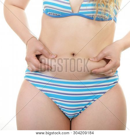 Overweight young woman shows belly fat, isolated over white background. Overeating xl size girl dressed in swimsuit unhappy with her figure and overweight