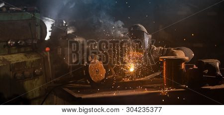 Welder is welding metal part in industrial workshop.