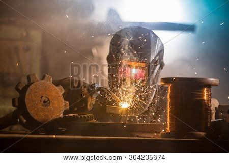 Welder is welding metal part in industrial workshop.