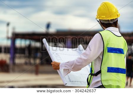 Woman Engineers Wear Safety Hats And Hold Blueprints In Their Hands.