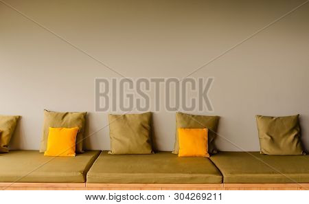 A Backless Seat Sofa With Five Square Khaki Pillows And Two Bright Yellow Pillows. Copy Space