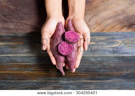 Purple Sweet Potatoes Holding By Hand On Wooden Background