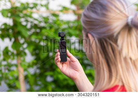 Young Blonde Woman Holding Osmo Camera For Vlogging Outdoor , Green Background