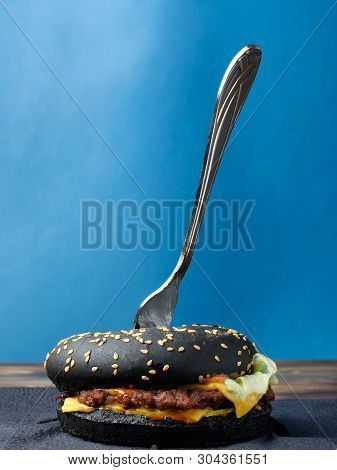 Black Hamburger With Fork On A Blue Background.