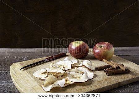Front View Dried Apple Chips , Raw Apple , Cinnamon Sticks On Cooking Board Over Wood Background.