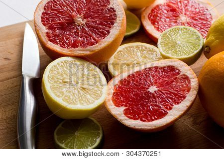Sliced Fresh Citrus (lemons, Limes, Grapefruits) On A Wooden Board With A Metal Knife, Side View