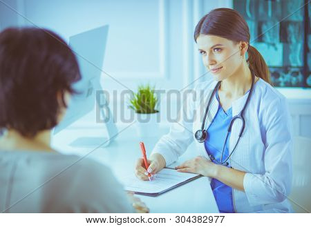 Doctor and patient discussing medical problems in a hospital consulting room. Doc filling in a patient's form