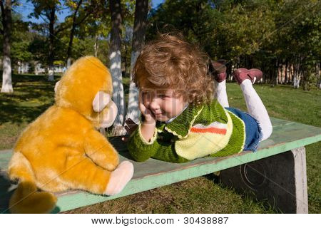 La petite fille pose sur un banc et « écoute » le singe de jouet.