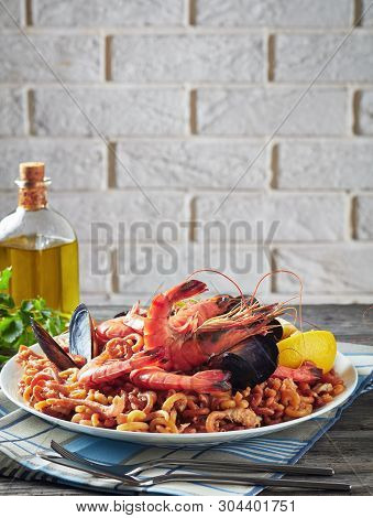 Spanish Fideua, A Noodle Paella With Prawns, Fish, Calamari, Mussels Served On A White Plate On A Gr