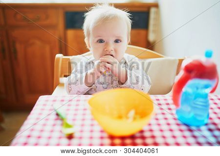 Cute Baby Girl Eating Lunch In The Kitchen. Little Kid Tasting Solids At Home. Baby Led Weaning