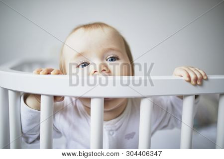 Adorable Baby Girl In Co-sleeper Crib Attached To Parents Bed. Little Kid Sitting In Cot