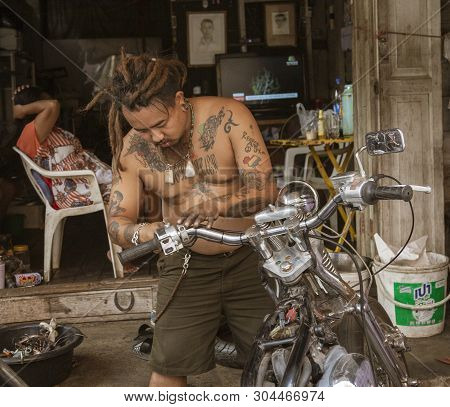 Lampeng, Tahiland - 2019-03-07 - Man With Many Tattoos Repairs His Motorcycle.