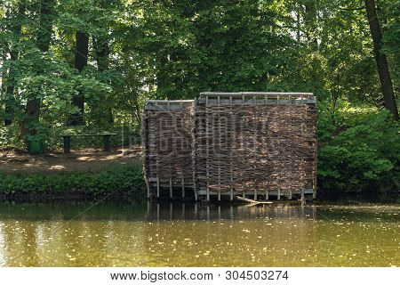 Wooden Building On The Shore Of The Pond. Wicker Building In The Forest.