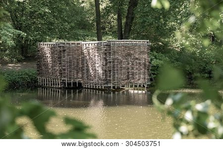 Wooden Building On The Shore Of The Pond. Wicker Building In The Forest.