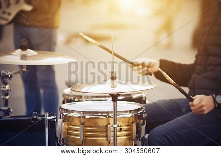 A Street Musician, Dressed In A Black Jacket And Blue Jeans, With A Watch On His Hand, Plays A Drum 