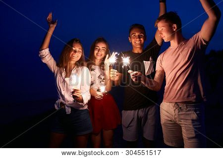 Friends Walking, Dancing And Having Fun During Night Party At The Seaside With Bengal Sparkler Light