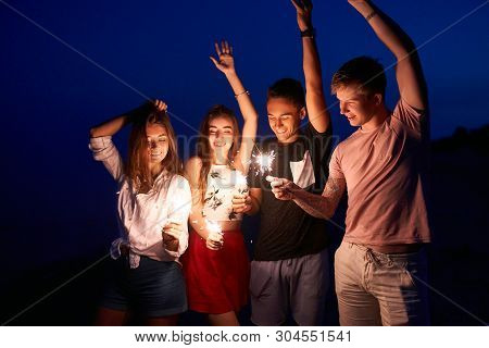 Friends Walking, Dancing And Having Fun During Night Party At The Seaside With Bengal Sparkler Light