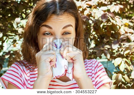 Young Girl With Allergy In Autumn Park. Sneezing Girl Blows Her Nose In A Napkin