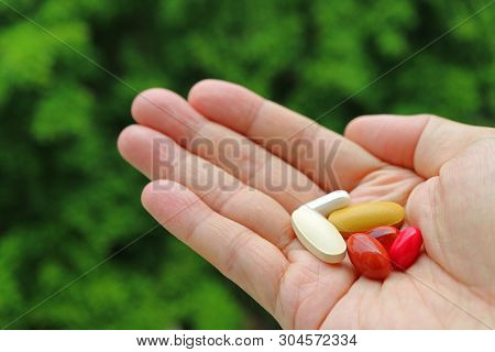 Assorted Supplement Pills In Man Palm With Blurry Green Foliage In Background