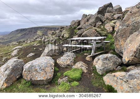 Wooden Picnic Table Sits On The Rocks Overlooking The Mountains In The Background With Rock Cliffs. 