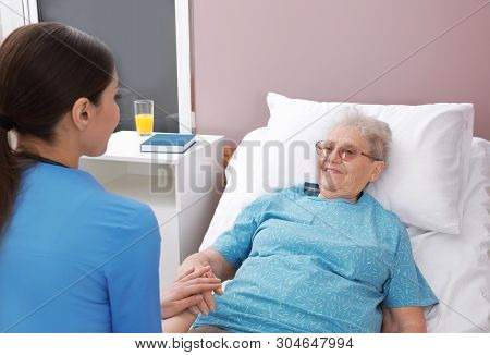 Nurse Assisting Senior Woman Lying On Bed In Hospital Ward