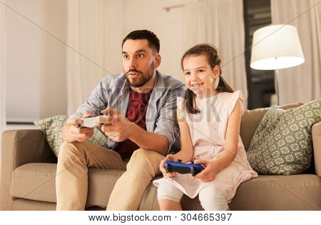 family, gaming and entertainment concept - happy father and little daughter with gamepads playing video game at home