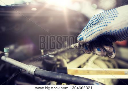 car service, repair, maintenance and people concept - auto mechanic man with dipstick and lamp checking for motor oil level at workshop