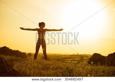 Young Woman Doing Stretching Outdoor. Warm up Exercise Against a Hot Beautiful Summer Sunset. Sport and Healthy Active Lifesyle Concept.