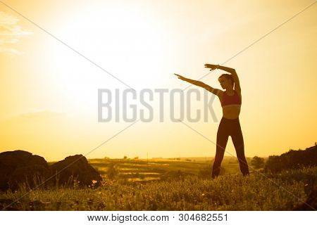 Young Woman Doing Stretching Outdoor. Warm up Exercise Against a Hot Beautiful Summer Sunset. Sport and Healthy Active Lifesyle Concept.