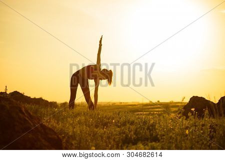 Young Woman Doing Stretching Outdoor. Warm up Exercise Against a Hot Beautiful Summer Sunset. Sport and Healthy Active Lifesyle Concept.