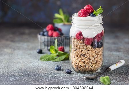 Granola Parfait With Yogurt, Oat Granola, Fresh Berries, Honey And Mint Leaves In Tall Glass Jar, Co