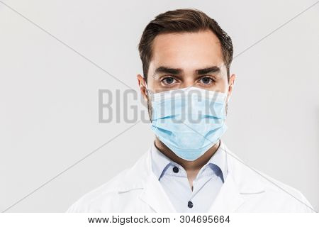 Portrait of european young medical doctor wearing sterile mask working in clinic laboratory and looking at camera isolated over white background