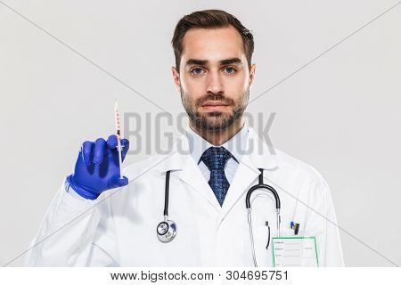 Portrait of european young medical doctor wearing disposable sterile gloves working in hospital and holding syringe isolated over white background