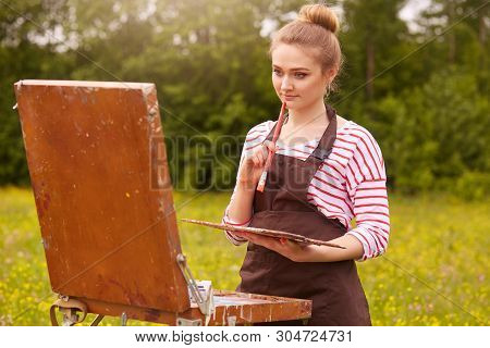 Horizontal Shot Of Young Woman Artist Painting Picture Using Sketchbook, Girl Enjoying Beautiful Nat