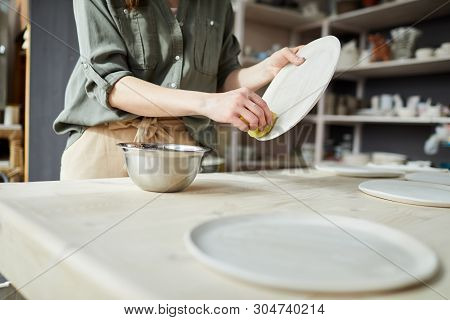 Mid Secion Portrait Of Unrecognizable Young Woman Finishing Handmade Ceramic Plate In Pottery Worksh