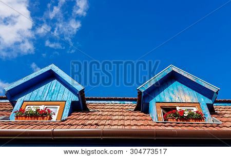 Windows With Flowers On Residentual House Rooftop, Blue Sky With White Clouds Background.