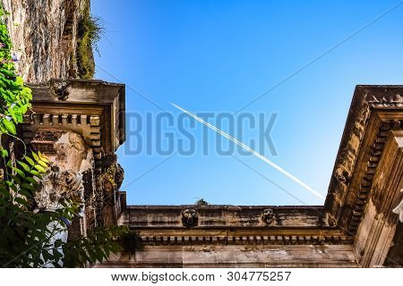 The Plane Leaving A Condensation Trail Flies High Above The Gates Of Hadrian. Adrian Gate, Antalya L