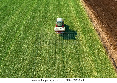 Unrecognizable Farmer In Agricultural Tractor Is Fertilizing Wheat Crop Field With Npk Fertilizers, 