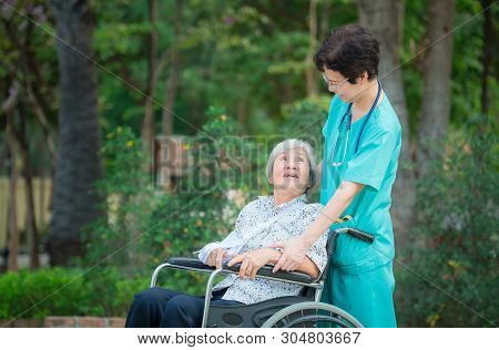 Smiling Caregiver Senior Nurse Take Care A Senior Patient On Wheelchair For Relaxing And Looking Aro