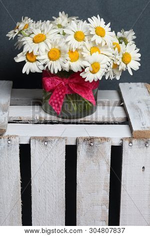 A Bouquet Of Field Daisies In A Glass Vase. On The  Wooden Box. Genus Of Perennial Flowering Plants