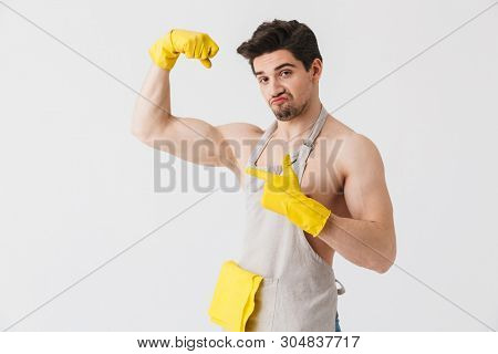 Handsome shirtless brunette houseman wearing apron standing isolated over white background, flexing muscles