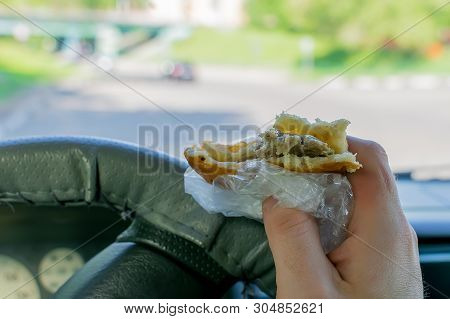 Pie, Belyash With Meat In The Hand Of The Driver In The Car On The Background Of The Steering Wheel 