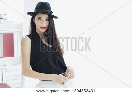 Sexy Asian Model Woman In Black Shirt And White Pants, Wearing Hat, Standing And Pompous, Studio Sho